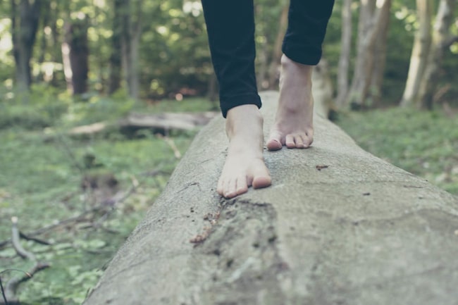 Frau balanciert mit nachkten Füßen auf einem Baumstamm