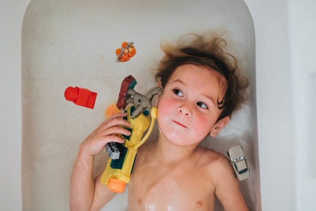 Kleiner Junge liegt in der Badewanne mit Spielzeug