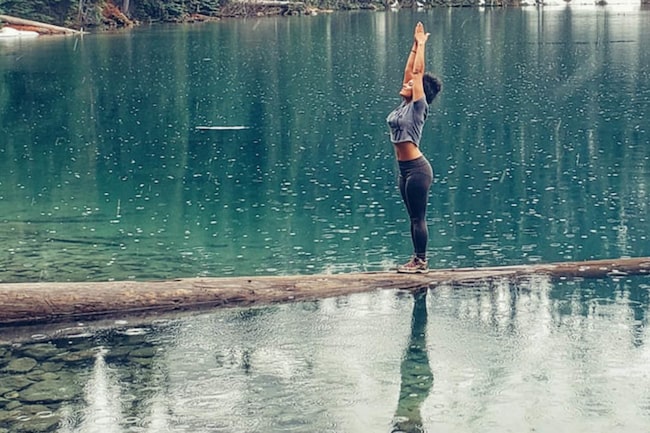 Frau macht Yogaübung auf einem Baumstamm im See
