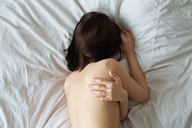 Frau liegt nackt in einem Bett am Bauch