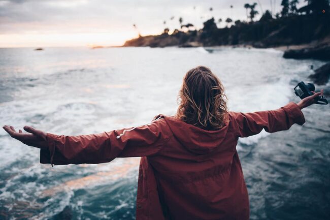 Frau steht mit offenen Armen am Meer