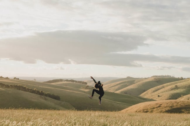 Mann springt in einem Weizenfeld in den Bergen in die Luft