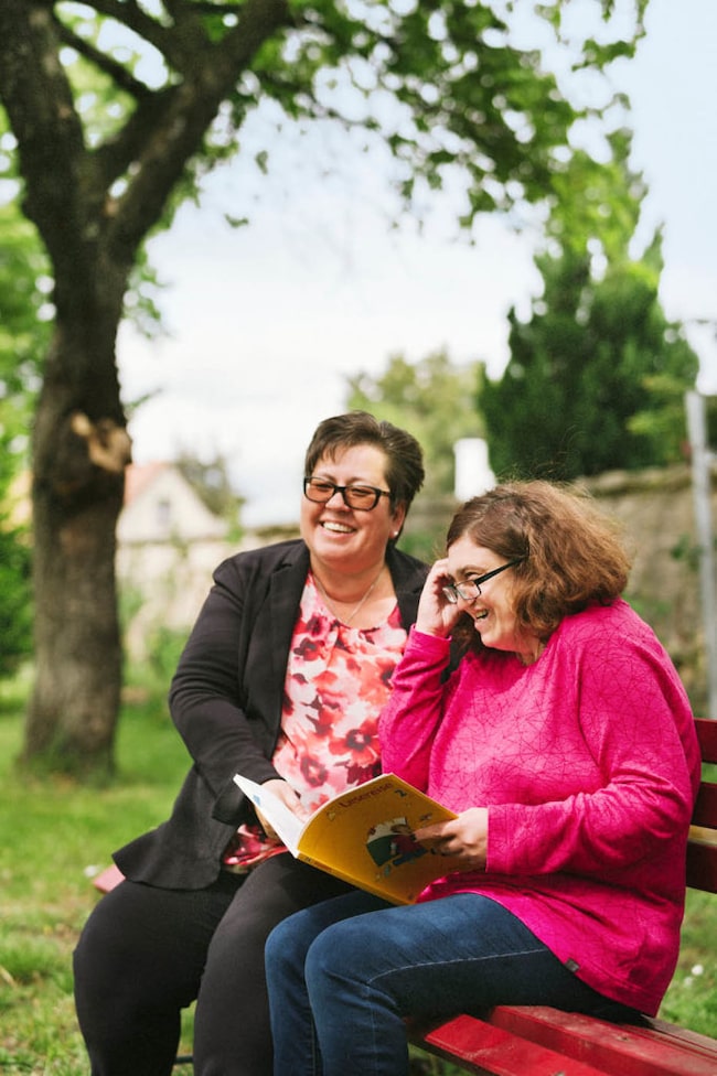Menschen helfen: Zwei Frauen sitzen lachend auf einer Bank