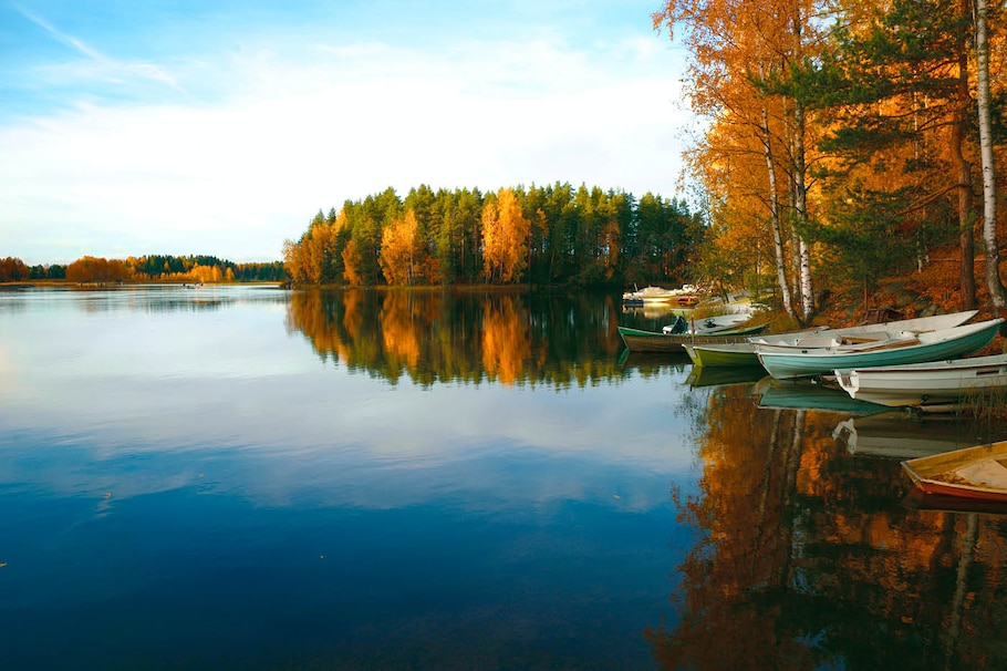 Auszeit nehmen: Herbstlicher See-Wald-Blick mit Booten am Wasser.