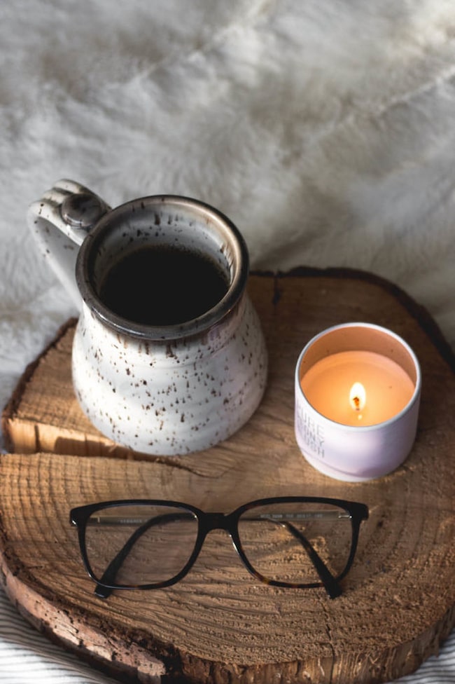 Brennende Kerze mit einer Tasse und Brille auf einem Holzbrett