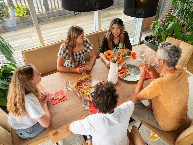 Familie sitzt am Esstisch und isst Pizza