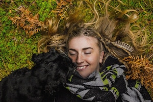 Frau und Hund im Herbst lachend auf Wiese.