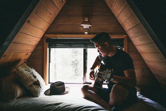 Mann auf Bett spielt Gitarre