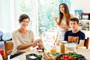 Familie sitzt rund um einen Küchentisch mit natürlichen Lebensmitteln