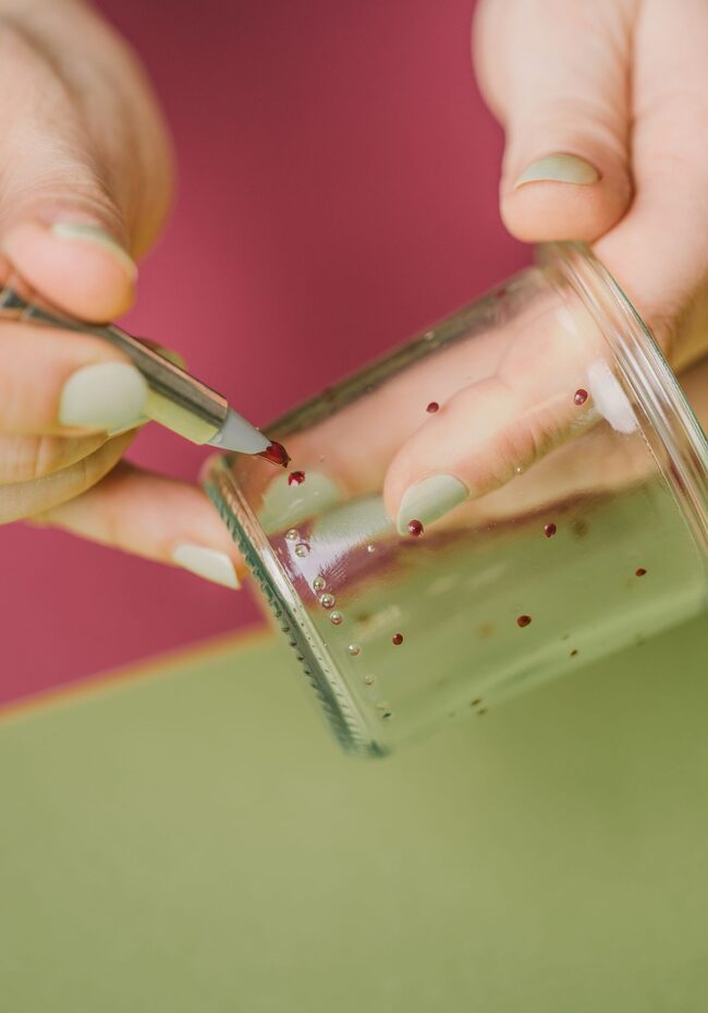 Frauenhände bemalen ein Glas mit zarten Punkten.