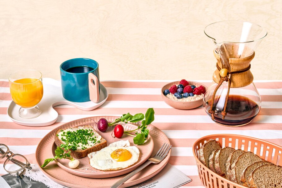 Frühstück, Frühstückstisch, Kaffeekanne, Kaffeetasse, Orangensaft, Butterbrot mit Schnittlauch, Spiegelei, Radieschen, Porridge mit Himberren und Heidelbeeren, Schwarzbrot, Teller, Gabel, Brot, Brotkorb, Zeitschrift, Brille, Ernährung