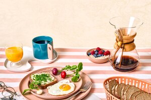 Frühstück, Frühstückstisch, Kaffeekanne, Kaffeetasse, Orangensaft, Butterbrot mit Schnittlauch, Spiegelei, Radieschen, Porridge mit Himberren und Heidelbeeren, Schwarzbrot, Teller, Gabel, Brot, Brotkorb, Zeitschrift, Brille, Ernährung