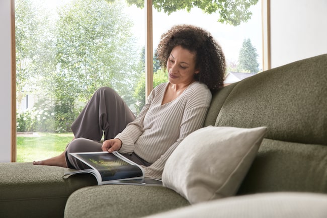 Frau sitzt auf grünem Sofa und liest ein Magazin