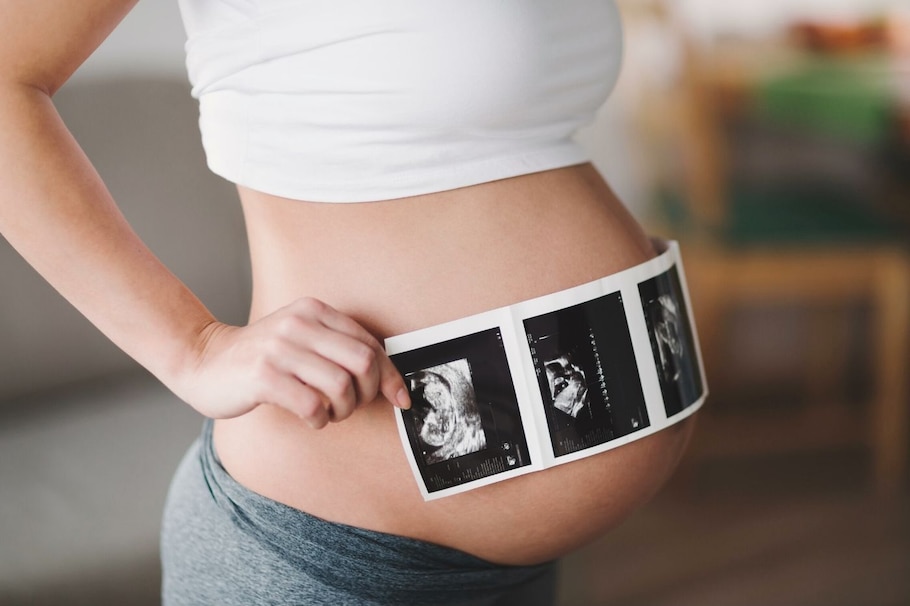 Phasen der Schwangerschaft: Frau mit Ultraschallbildern vorm Babybauch gehalten