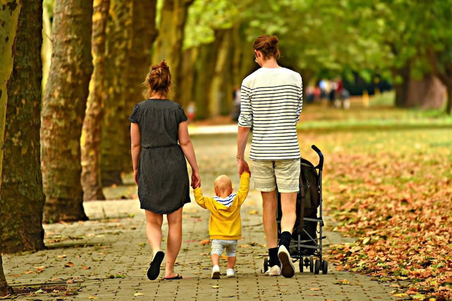 Alle Eltern erziehen unterschiedlich: Paar hält Kleinkind an den Händen auf herbstlicher Allee