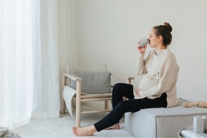 Frau in der Schwangerschaft mit Erkältung trinkt Tee am Sitzpouf