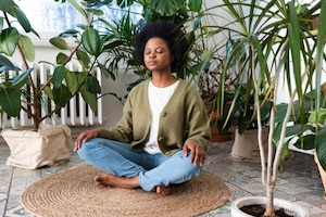 Bewusste Herzatmung: Frau bei Meditation daheim, umringt von Zimmerpflanzen