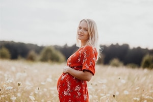 Mama werden: Schwangere Frau in rotem Kleid im Kornfeld