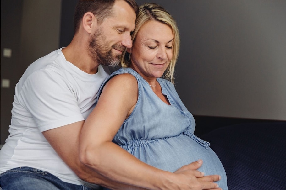 Schwanger mit 40: Mann umarmt schwangere Frau mit Babybauch von hinten