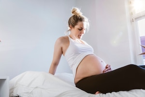Frau mit blankem Babybauch auf Bett: Eine Eipollösung kann am Ende der Schwangerschaft die Geburt einleiten