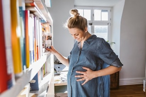 Schwangere Frau vorm Bücherregal mit Hand auf Bauch kurz vor den Wehen