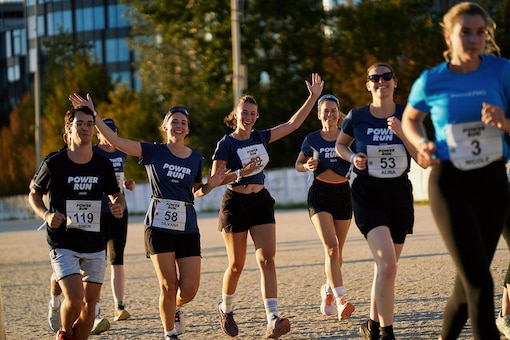 Läuferinnen und Läufer des POWER RUN laufen gemeinsam auf der Trabrennbahn und halten ihre Hände in die Höhe.