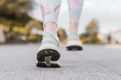Zwei Paar Laufschuhe auf Asphalt, die eine laufende Bewegung nachahmen.