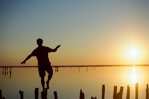 Mann balanciert auf Pfählen im See im Sonnenuntergang.