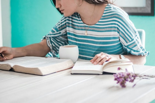 Frau sitzt an Tisch mit 2 Büchern und liest