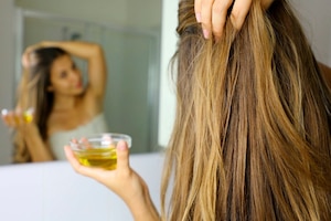 Frau vorm Badezimmerspiegel beruhigt mit Öl ihre juckende, schmerzende Kopfhaut