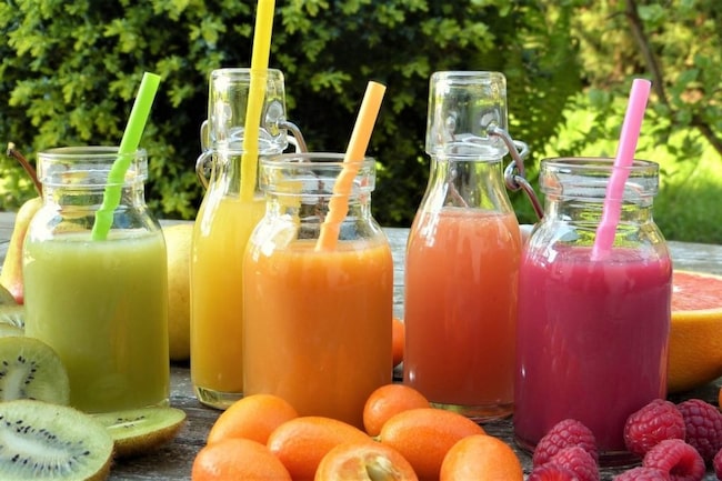 Saftkur mit vielen bunten frischgepressten Smoothies in Glasflaschen und Strohhalm