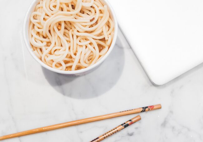 Nudelsuppe neben Laptop und Essstäbchen