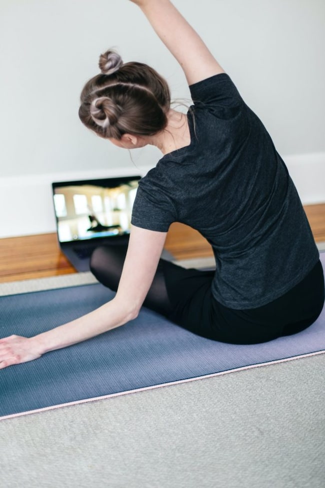 Frau macht Yoga am Boden vor dem Laptop