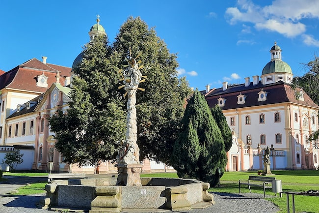 Das Zisterzienserinnenkloster St. Marienthal in Ostritz: Ansicht auf den Brunnen mit Pestsäule an einem strahlend sonnigen Tag.