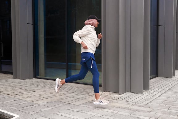 Frau in Running-Outfit läuft an einem Haus mit Glasfront im urbanen Ambiente vorbei.