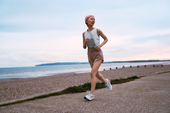 Junge Frau mit rosa Haaren und sportlichem Outfit läuft über eine Strandpromenade