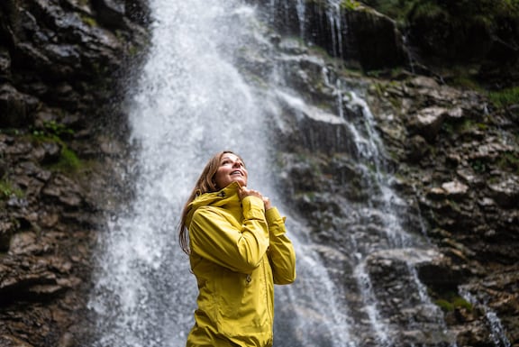 Frau mit gelbem Regenmantel steht vor einem Wasserfall