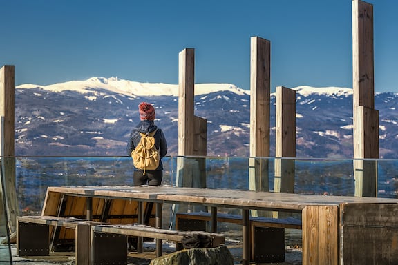 Eine Wanderin auf der Terrasse einer Bergstation am Panoramasteg im Sausal. Im Hintergrund sieht man schneebedeckte Berggipfel.