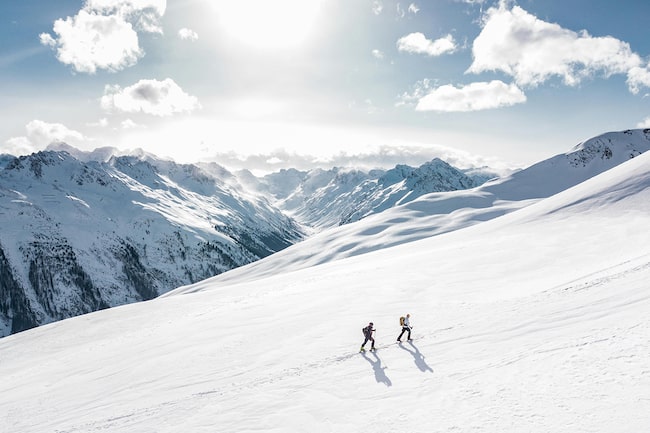 Zwei Skitourengeher auf ihrem Weg auf einen verschneiten Gipfel in den österreichischen Alpen.