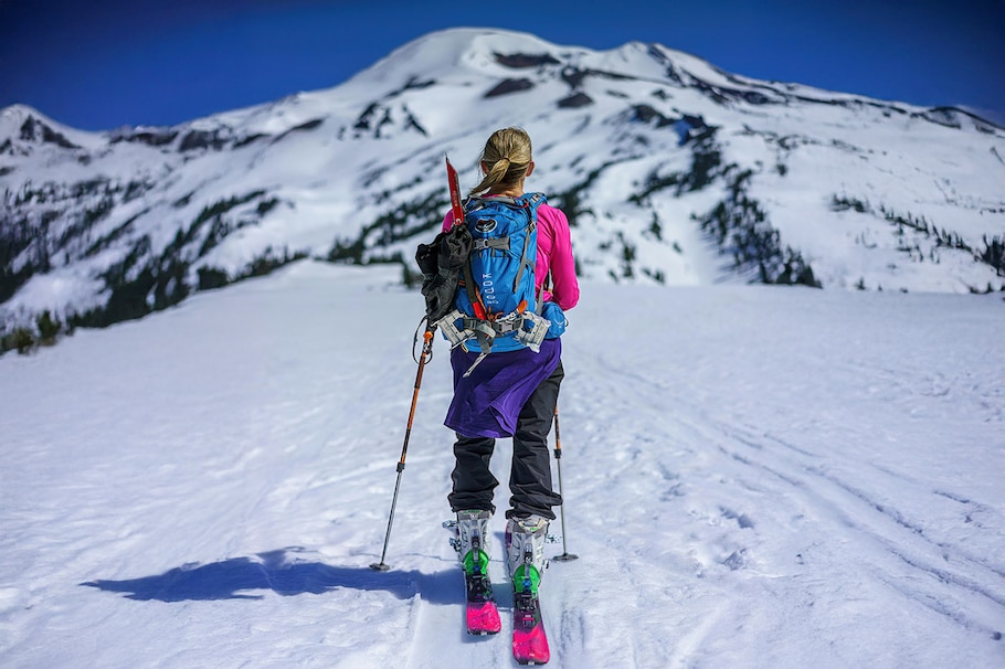 Eine Skitourengeherin auf dem Weg durch eine verschneite Berglandschaft in knallig bunter Bekleidung.