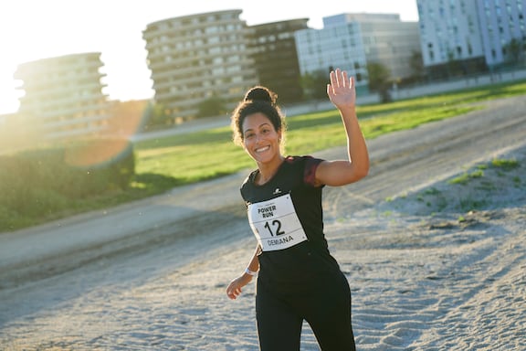 Eine Teilnehmer des POWER RUN winkt mit einem Lächeln im Gesicht.