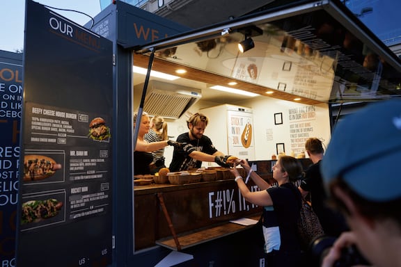 Teilnehmerinnen und Teilnehmer holen sich beim Foodtruck einen Burger.