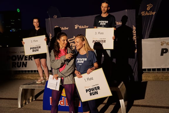 Alina Marzi interviewt eine Mitarbeiterin von Tchibo. Hinter ihnen stehen der Drittplatzierte und die Zweitplatzierte des POWER RUN.