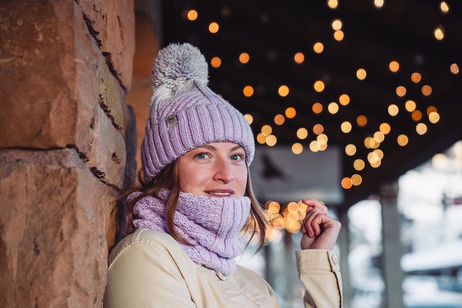Eine Frau trägt eine Beanie in der Farbe Grape Ice mit passenden Neckwarmer im Winter draußen.