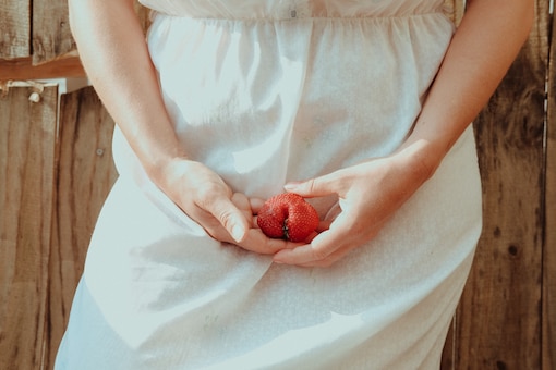 Detailaufnahme von einer Frau im weißen Kleid, die eine Erdbeere vor ihrem Schambereich in den Händen hält